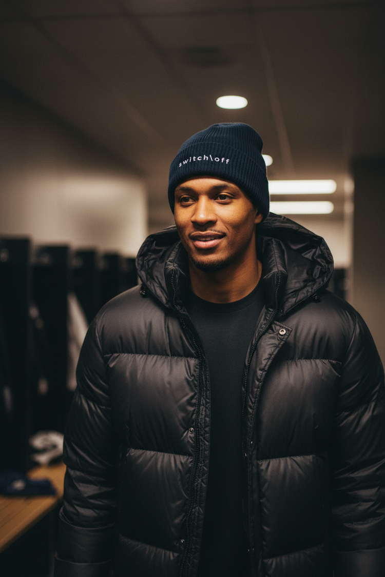An athlete leaving a locker room wearing a winter coat and the Organic Cuffed Ribbed beanie in navy with white switch\off embroidery | switch\off | An Athlete Trains